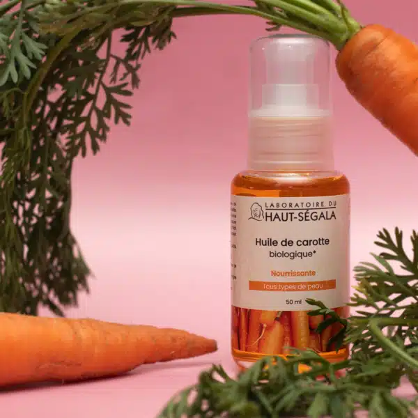 Flacon d'Huile de Carotte biologique 50ml du Laboratoire Haut-Ségala, entouré de carottes fraîches et de leurs fanes.