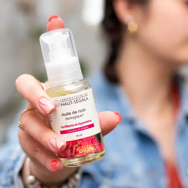 Main tenant un flacon d'Huile de Ricin biologique 50ml du Laboratoire Haut-Ségala, produit fortifiant pour cheveux et ongles.
