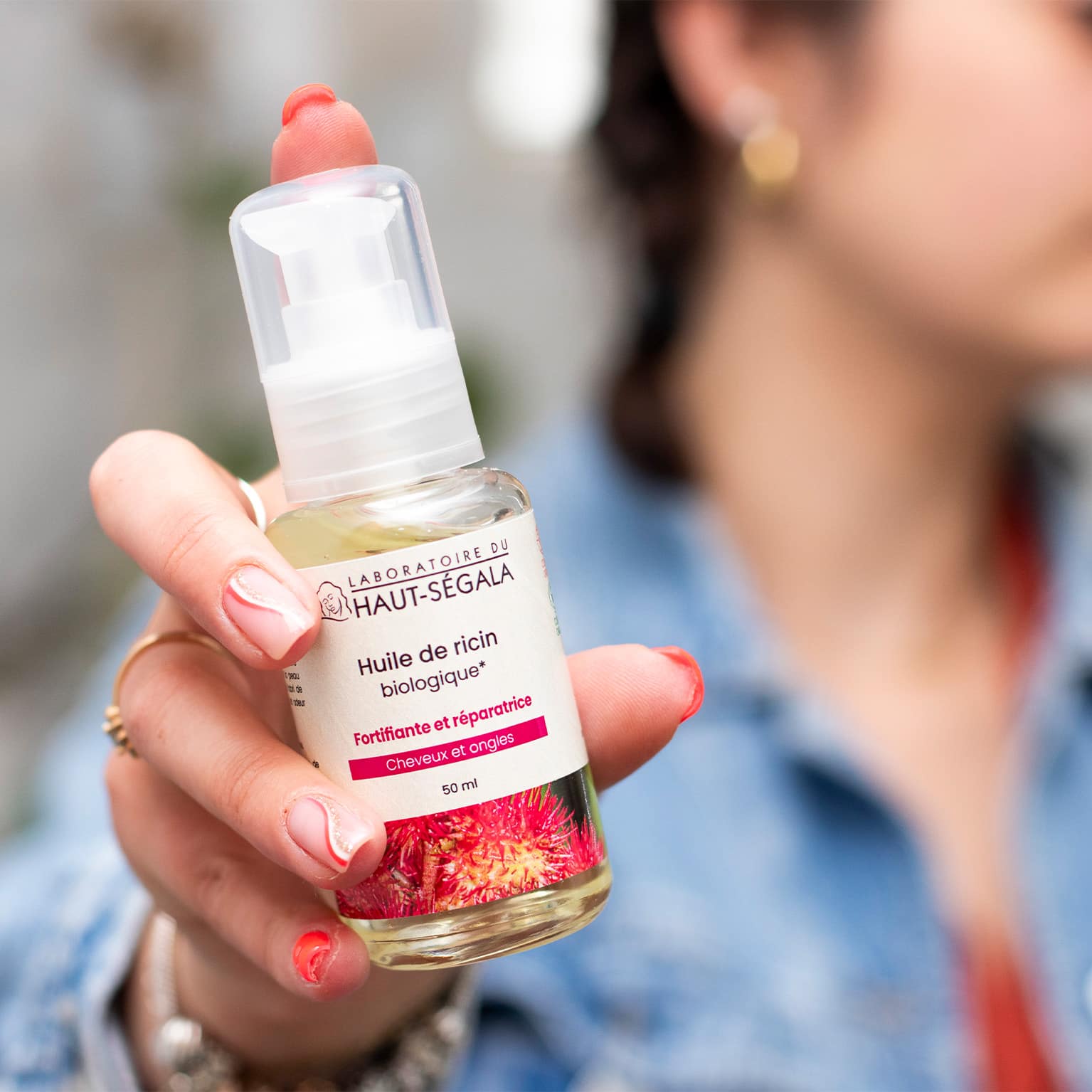Main tenant un flacon d'Huile de Ricin biologique 50ml du Laboratoire Haut-Ségala, produit fortifiant pour cheveux et ongles.