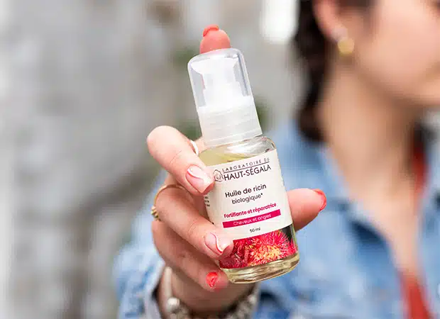 Main tenant un flacon d'Huile de Ricin biologique 50ml du Laboratoire Haut-Ségala, produit fortifiant pour cheveux et ongles.