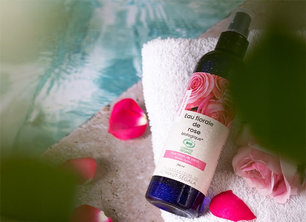 Flacon d'Eau Florale de Rose Biologique 250ml du Laboratoire Haut-Ségala, posé sur une serviette avec des pétales de rose.