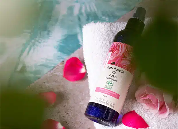 Flacon d'Eau Florale de Rose Biologique 250ml du Laboratoire Haut-Ségala, posé sur une serviette avec des pétales de rose.