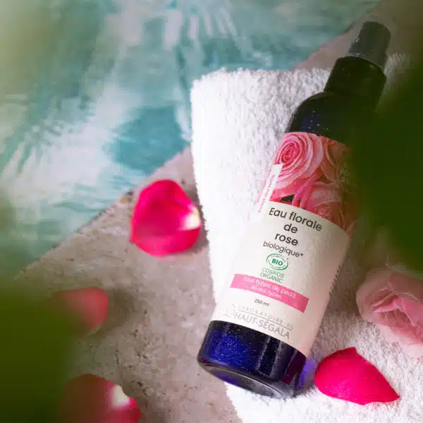 Flacon d'Eau Florale de Rose Biologique 250ml du Laboratoire Haut-Ségala, posé sur une serviette avec des pétales de rose.