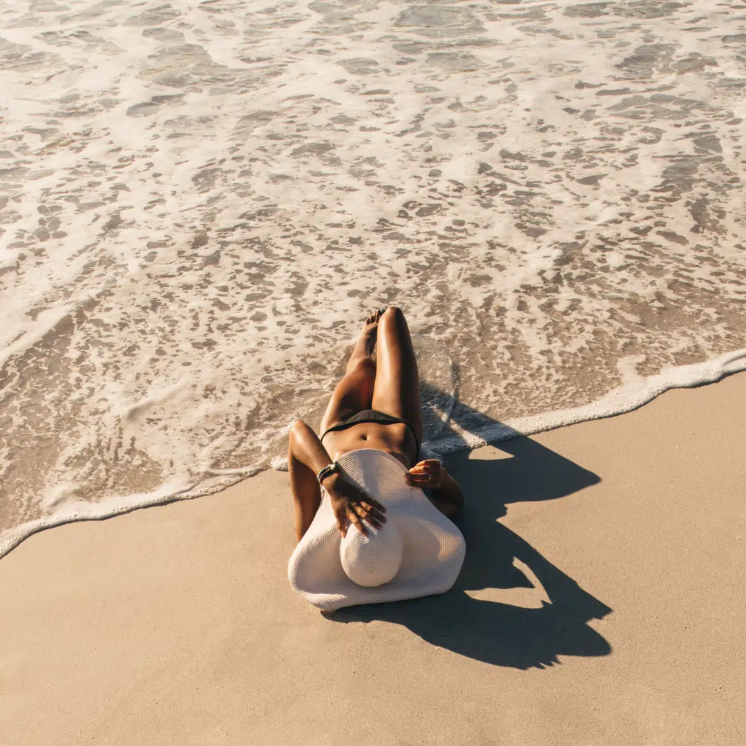 Femme allongée sur la plage après une exposition au soleil, symbolisant la détente et le besoin d'apaiser la peau.