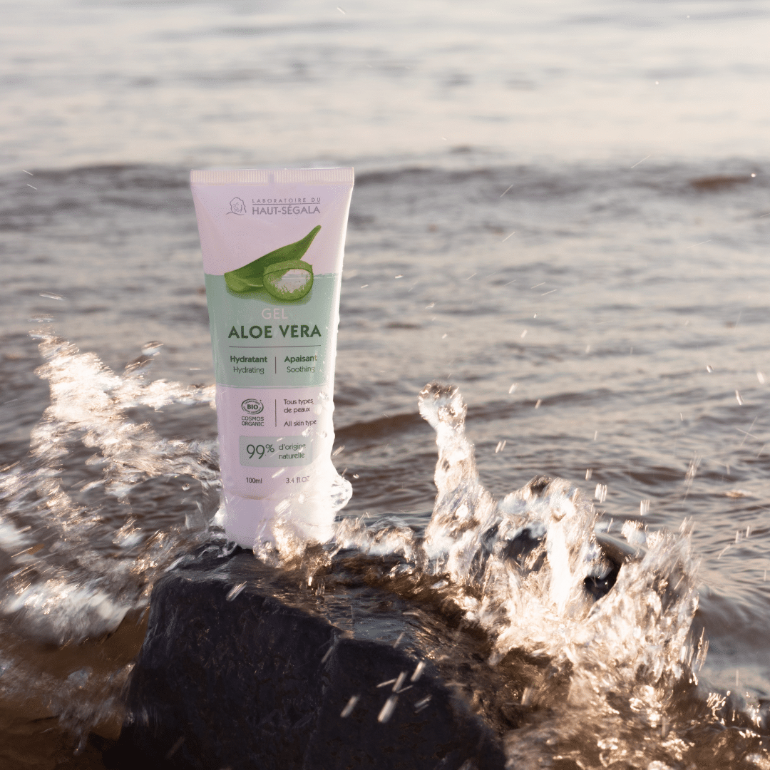 Tube de gel d'aloe vera posé sur une roche au bord de l'eau, parfait pour apaiser la peau après l'exposition solaire.