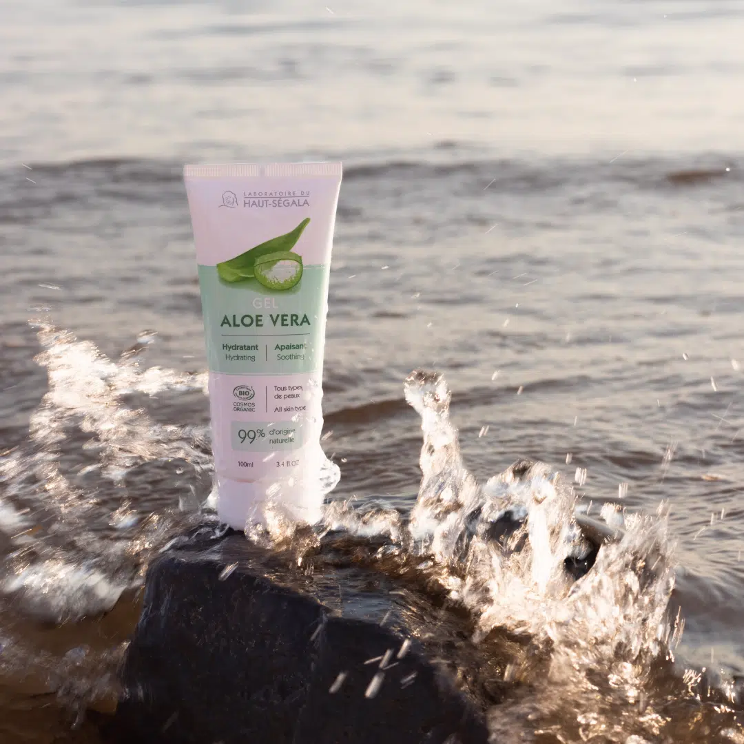 Tube de gel d'aloe vera posé sur une roche au bord de l'eau, parfait pour apaiser la peau après l'exposition solaire.