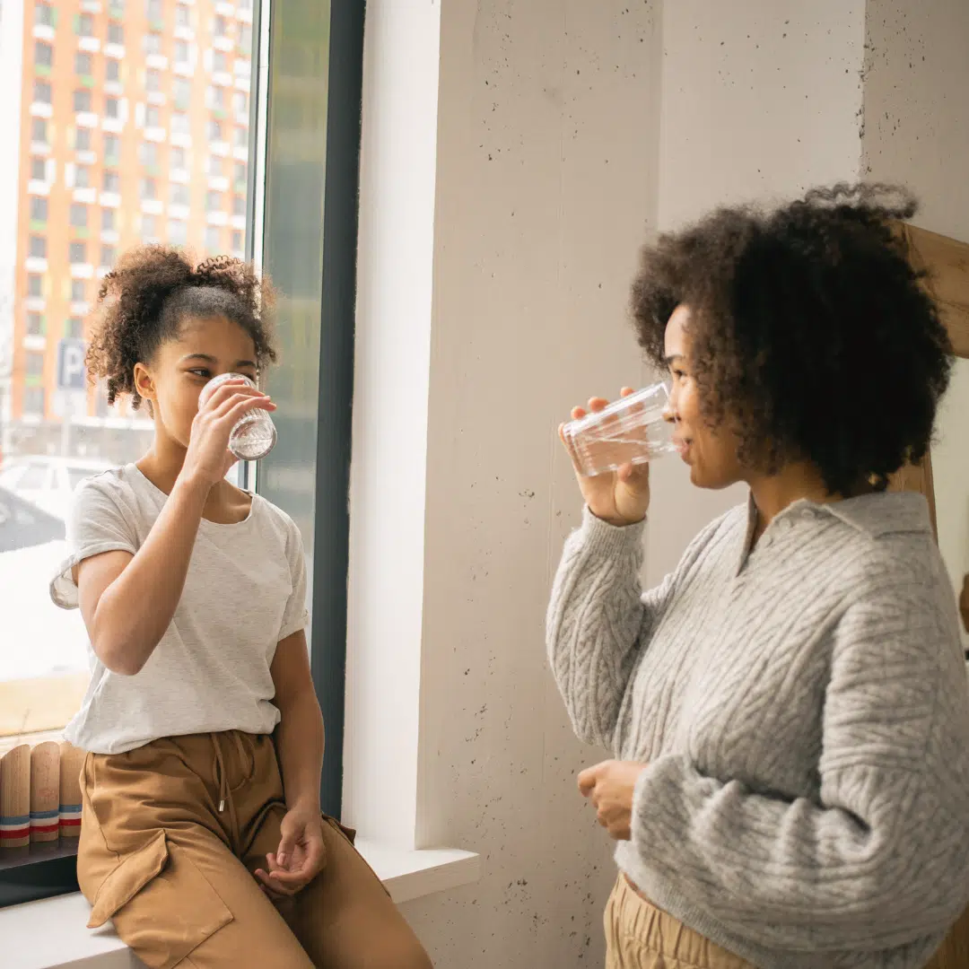 Deux femmes buvant de l'eau, symbolisant l'hydratation et l'apaisement de la peau après une exposition au soleil.