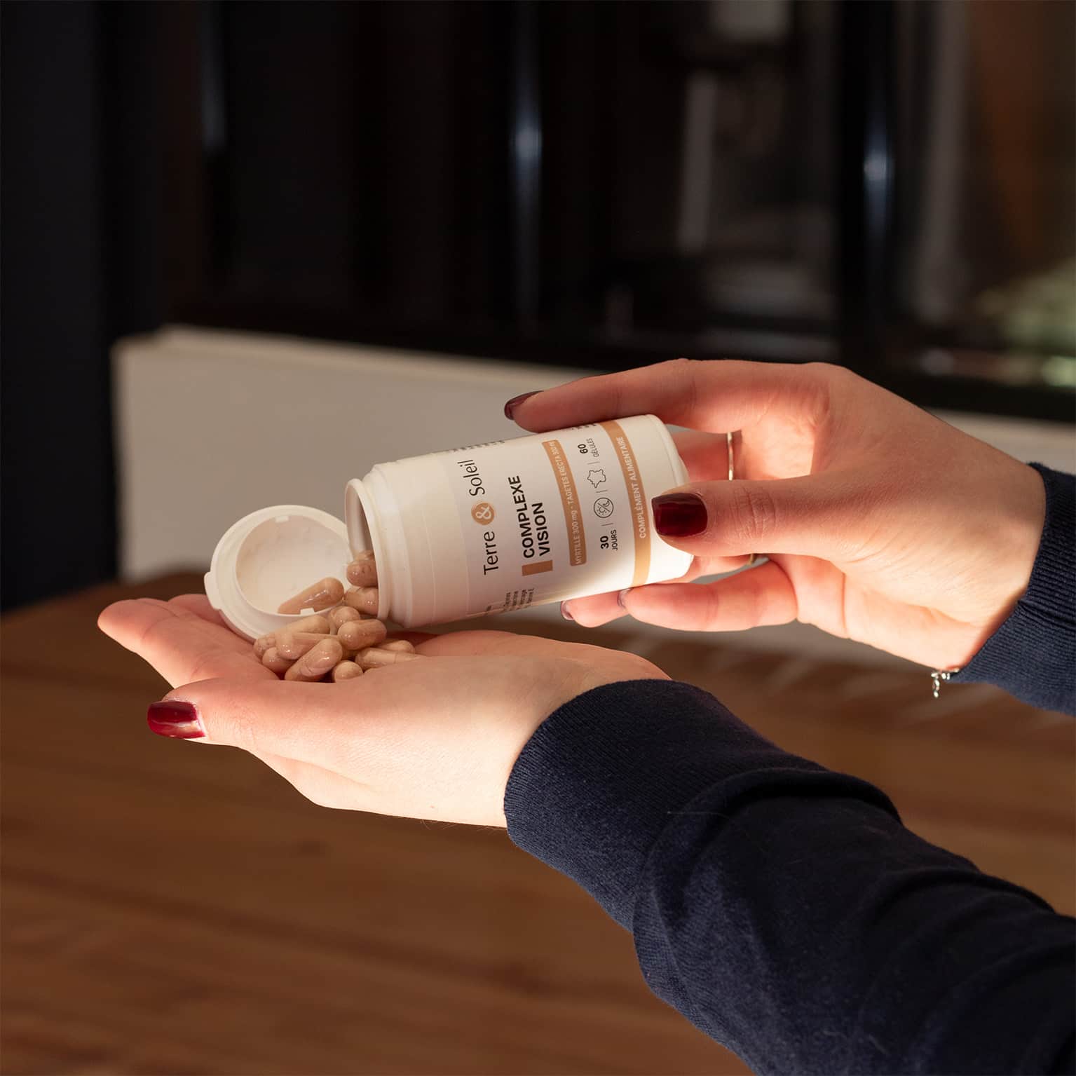 Une personne tient dans sa main une poignée de gélules du complément alimentaire "Complexe Vision" de Terre et Soleil, versées d'un flacon. L'étiquette indique "60 gélules" pour une cure de "30 jours" et un flacon de 50 ml.