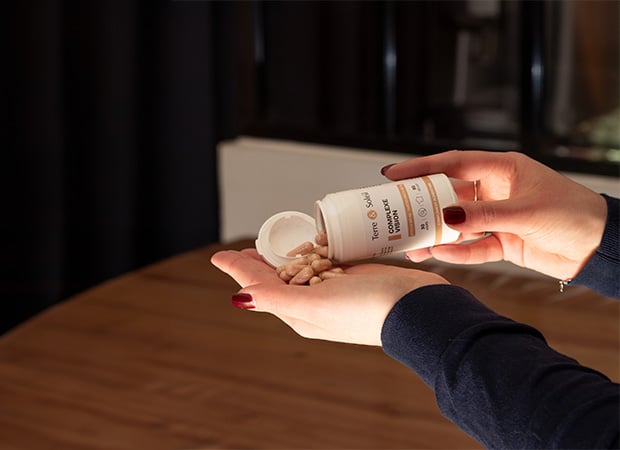 Une personne tient dans sa main une poignée de gélules du complément alimentaire "Complexe Vision" de Terre et Soleil, versées d'un flacon. L'étiquette indique "60 gélules" pour une cure de "30 jours" et un flacon de 50 ml.