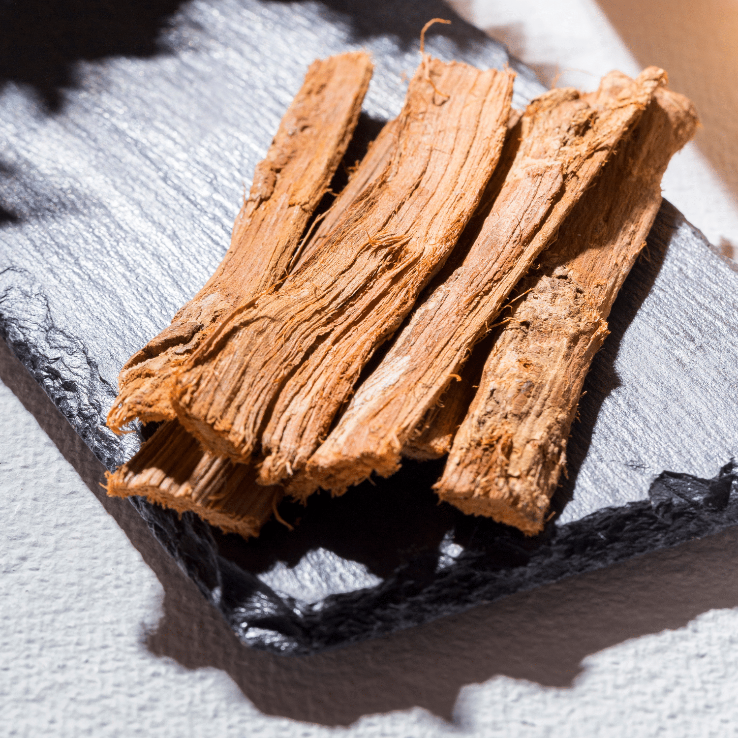 Plusieurs morceaux d'écorce séchée, de couleur marron clair, posés sur une surface foncée et texturée. Ces écorces sont des fragments de la griffe du chat écorce (Uncaria tomentosa), un ingrédient naturel complément utilisé en phytothérapie.