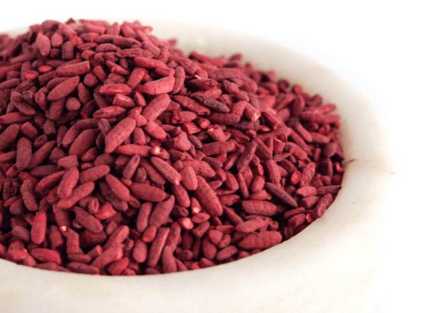 Un bol en pierre claire rempli de grains de riz rouge fermenté de couleur bordeaux. Les grains sont de forme allongée et ont une texture granuleuse. L'image met en évidence le riz rouge fermenté, un ingrédient naturel cholestérol.