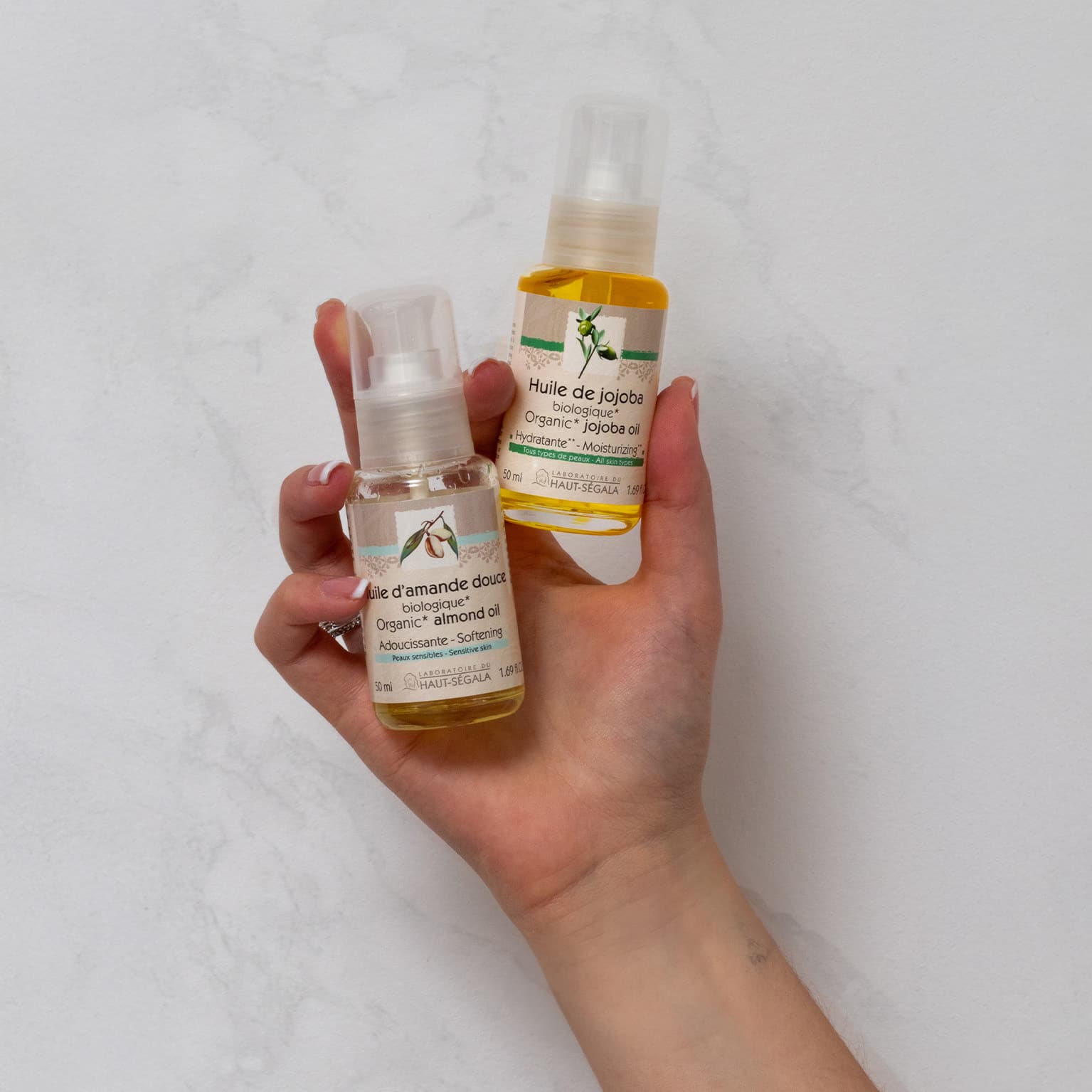 Main tenant deux flacons d'huiles végétales biologiques Haut-Ségala : Huile de Jojoba et Huile d'Amande Douce.