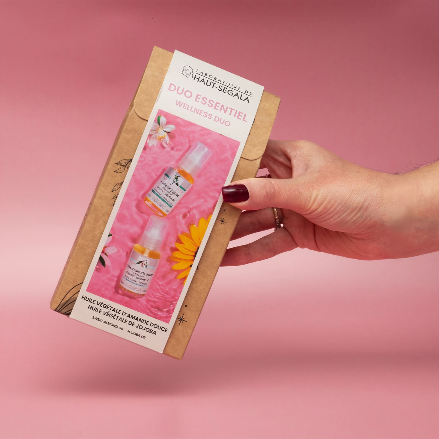 Main tenant un coffret "Duo Essentiel Wellness Duo" du Laboratoire Haut-Ségala, contenant des flacons d'huile d'amande douce et d'huile de jojoba biologiques.