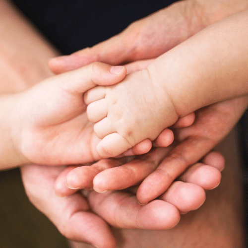Les mains de trois personnes d'âges différents (un adulte, un enfant et un bébé) sont empilées, symbolisant le soin naturel famille et la transmission du bien-être toutes générations. L'image évoque la douceur et la protection de la peau avec des produits doux peaux sensibles et des cosmétiques bio enfants.
